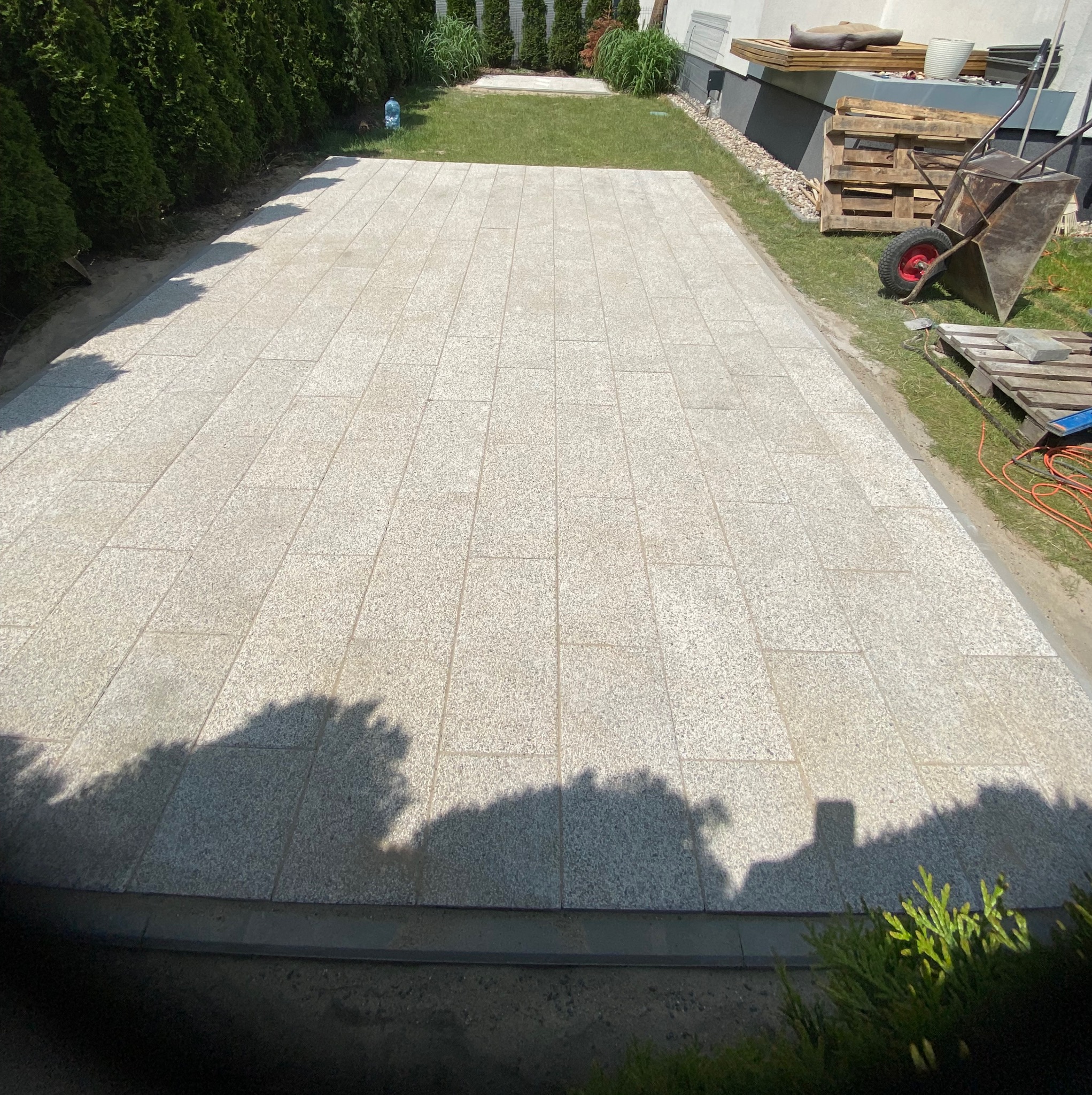 Ułożona jasnoszara nawierzchnia z prostokątnych płyt granitowych, widok z góry na gotowy podjazd, z widocznymi narzędziami i materiałami budowlanymi w tle.