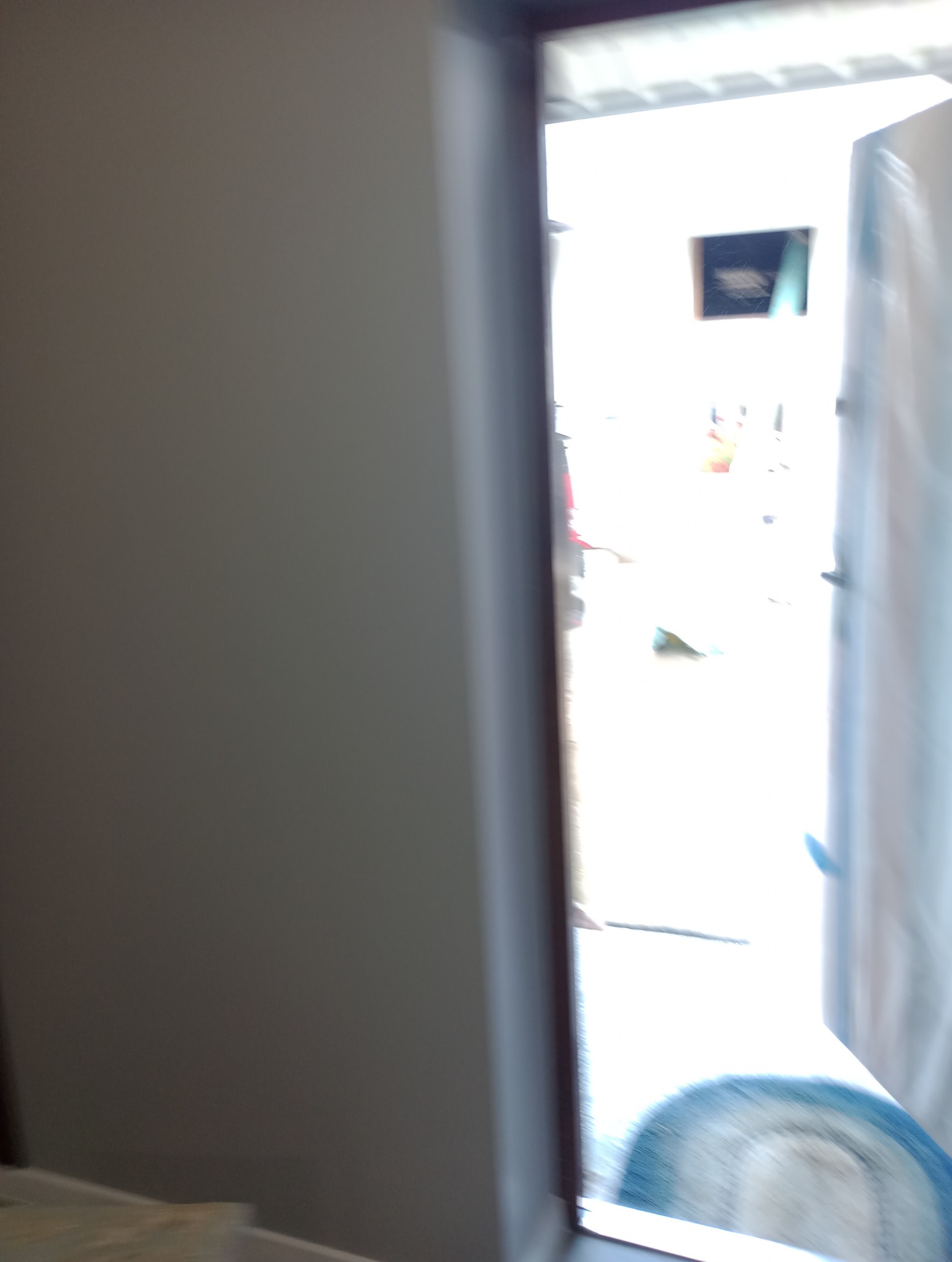 Fragment ściany i otwartych drzwi, widok na jasne pomieszczenie z elementami wyposażenia, zdjęcie zrobione w ruchu, niewyraźne