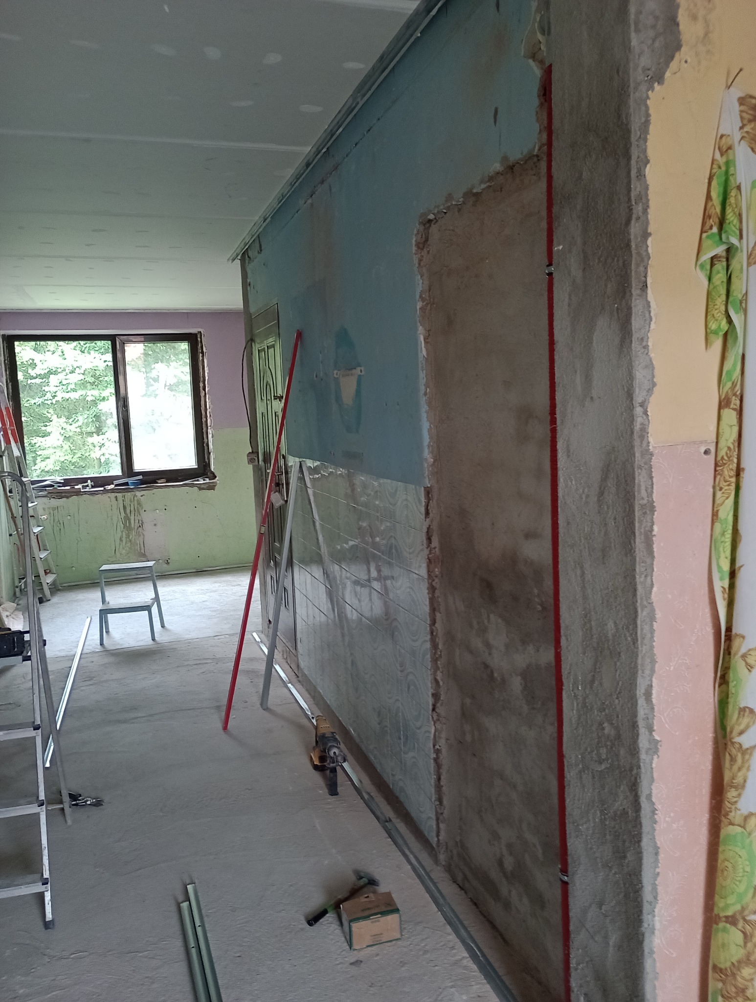 Przygotowanie ściany do montażu płyty karton gips: widoczne profile, narzędzia i fragmenty starej glazury w trakcie prac remontowych w pomieszczeniu z oknem.