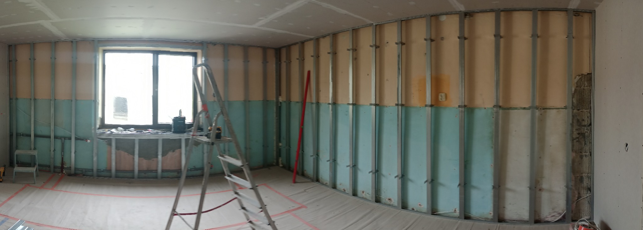 Wnętrze w trakcie prac przygotowawczych do montażu płyt kartonowo-gipsowych na metalowym stelażu, widoczna drabina, poziomica i laserowy niwelator na parapecie okna, podłoga zabezpieczona folią...