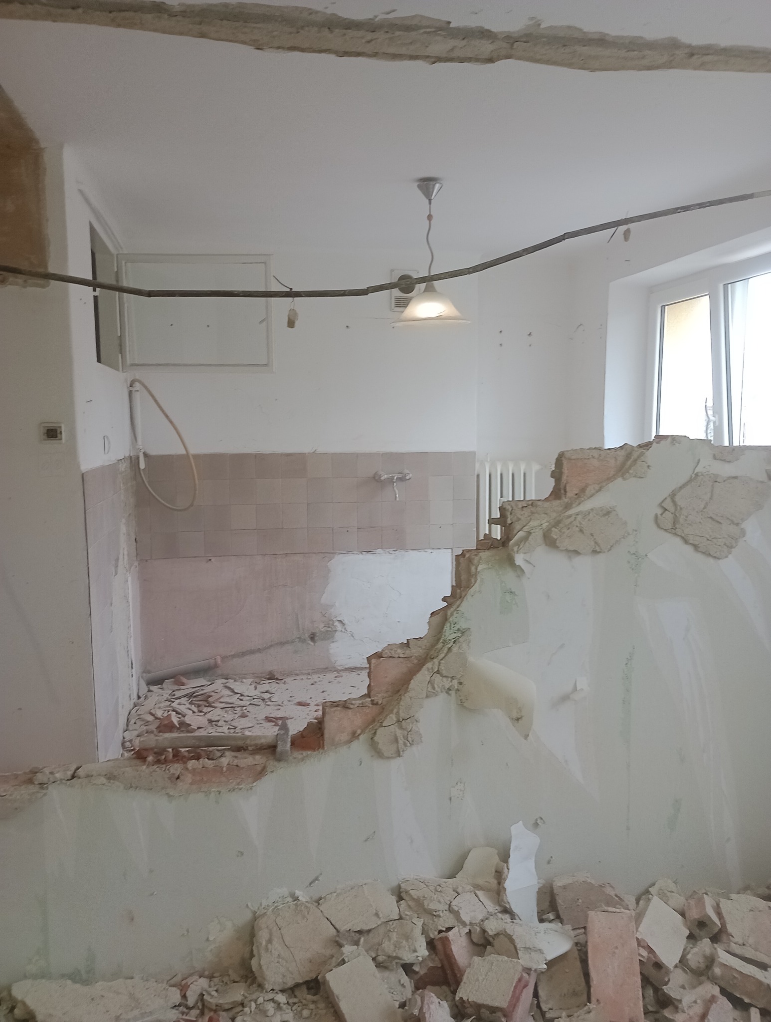 Demontaż ściany działowej w kuchni z widocznymi fragmentami płytek i instalacji, przygotowanie do remontu.