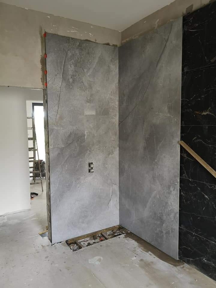 Montaż płytek imitujących marmur na ścianach w łazience, widoczny fragment instalacji elektrycznej, poziom podłogi nieukończony, płytki zabezpieczone pomarańczowymi elementami dystansowymi.