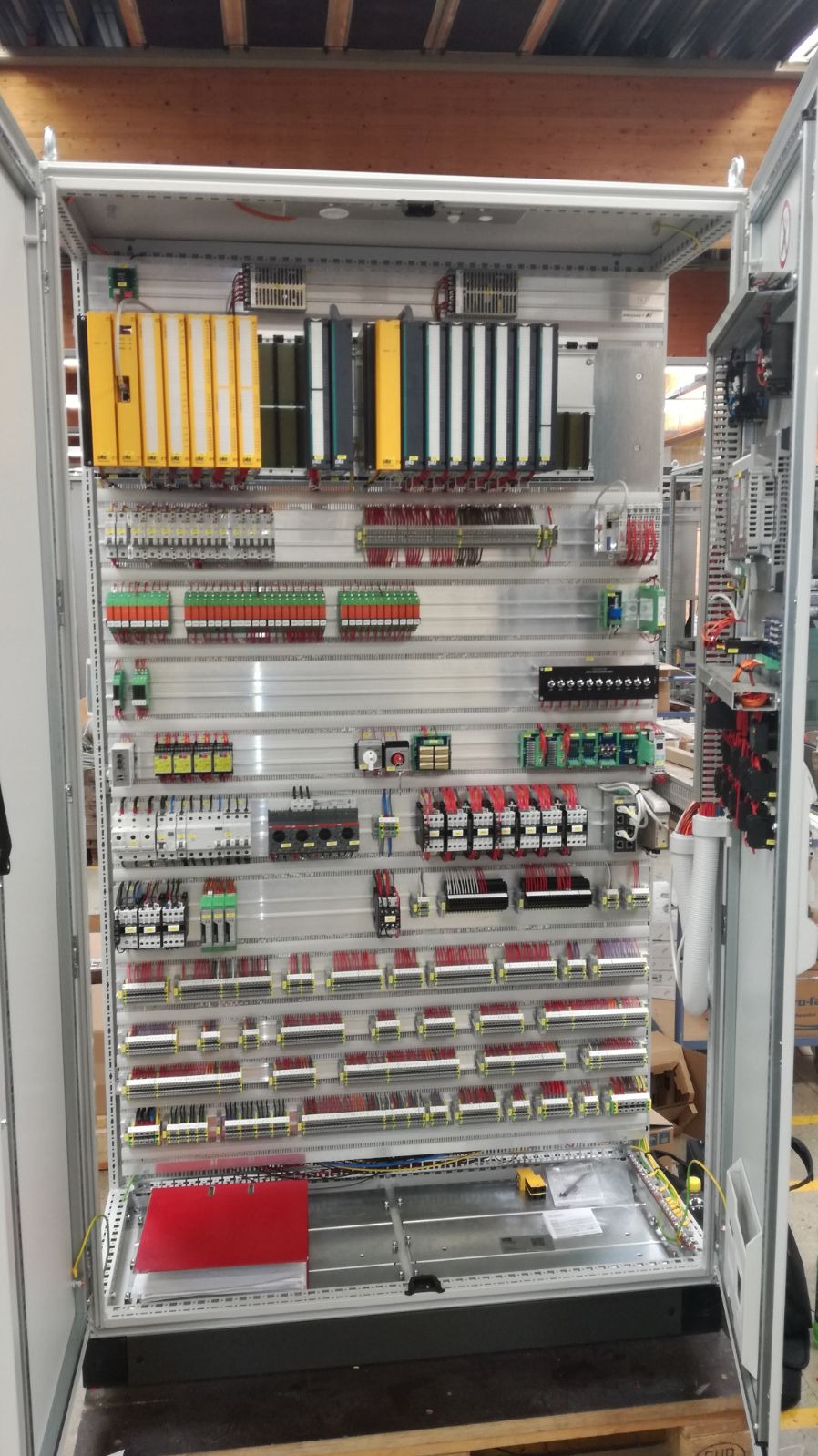 Otwarta szafa sterownicza z modułami, okablowaniem i zabezpieczeniami, zainstalowana przez elektryka w Katowicach. Widoczne liczne przewody w peszlach i listwach, złącza oraz elementy automatyki...