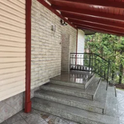 Zadaszone schody wejściowe z szarego granitu, z kutą balustradą. Kamienna elewacja budynku z kremową okładziną po lewej. Czerwona drewniana konstrukcja dachu.