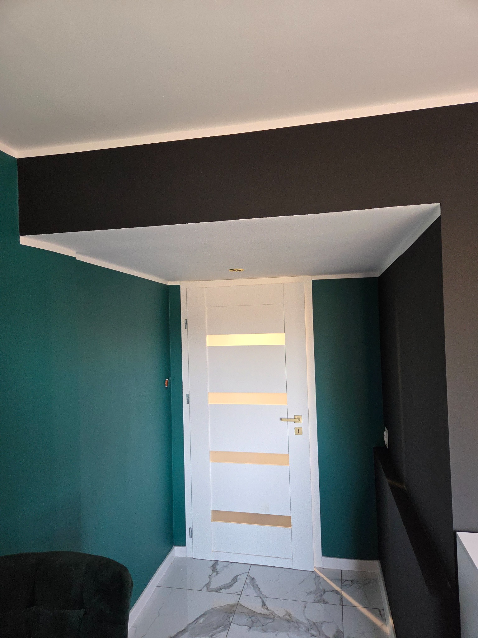Nowoczesne wnętrze z białą, przeszkloną stolarką drzwiową, pomalowane ściany w kolorze butelkowej zieleni i grafitu, marmurowe płytki podłogowe.