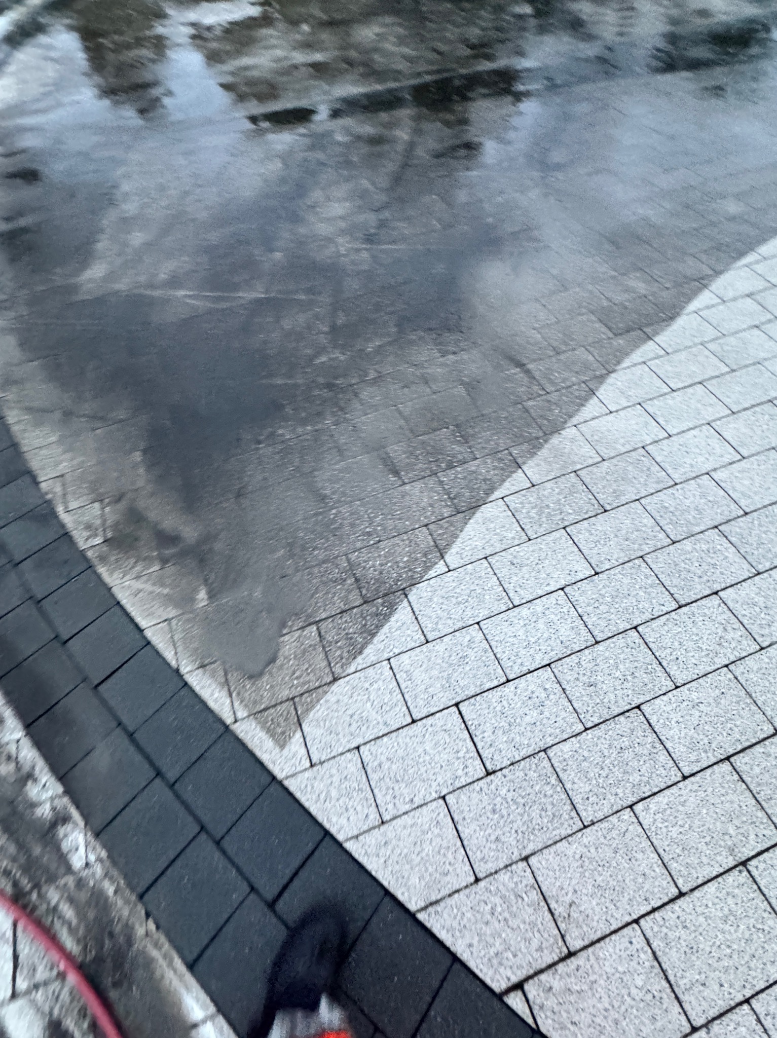 Częściowo umyta kostka brukowa, widoczna różnica między czystą, jasną powierzchnią a brudną, mokrą strefą. Ciemna obwódka z kostki po lewej stronie.