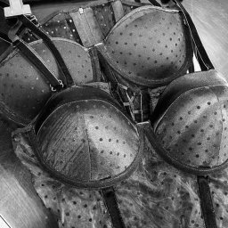 1LS Iryna Kozarenko - Czarno-białe zdjęcie biustonosza i gorsetu w drobne kropki, wiszących na wieszaku z metalowymi klipsami, widoczne fragmenty ekranu telefonu z tekstem w języku rosyjskim.