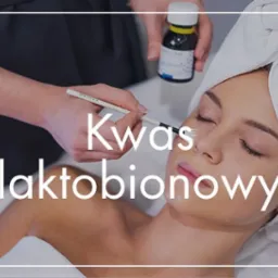 Aplikacja kwasu laktobionowego pędzlem na twarz kobiety z ręcznikiem na głowie, butelka z preparatem w tle.