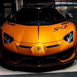 Myszyński Design Sp. z o. o. - Pomarańczowy Lamborghini Aventador SVJ, widok z przodu, z czarnymi akcentami i naklejkami, zaparkowany w garażu podziemnym.