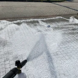 Pryskanie pianą czyszczącą na kostkę brukową za pomocą lancy pianowej, widoczny fragment kostki przed i po czyszczeniu.