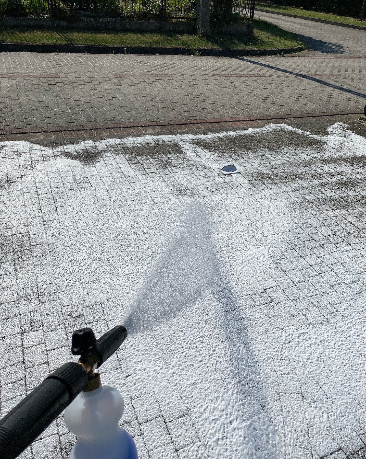 Pryskanie pianą czyszczącą na kostkę brukową za pomocą lancy pianowej, widoczny fragment kostki przed i po czyszczeniu.