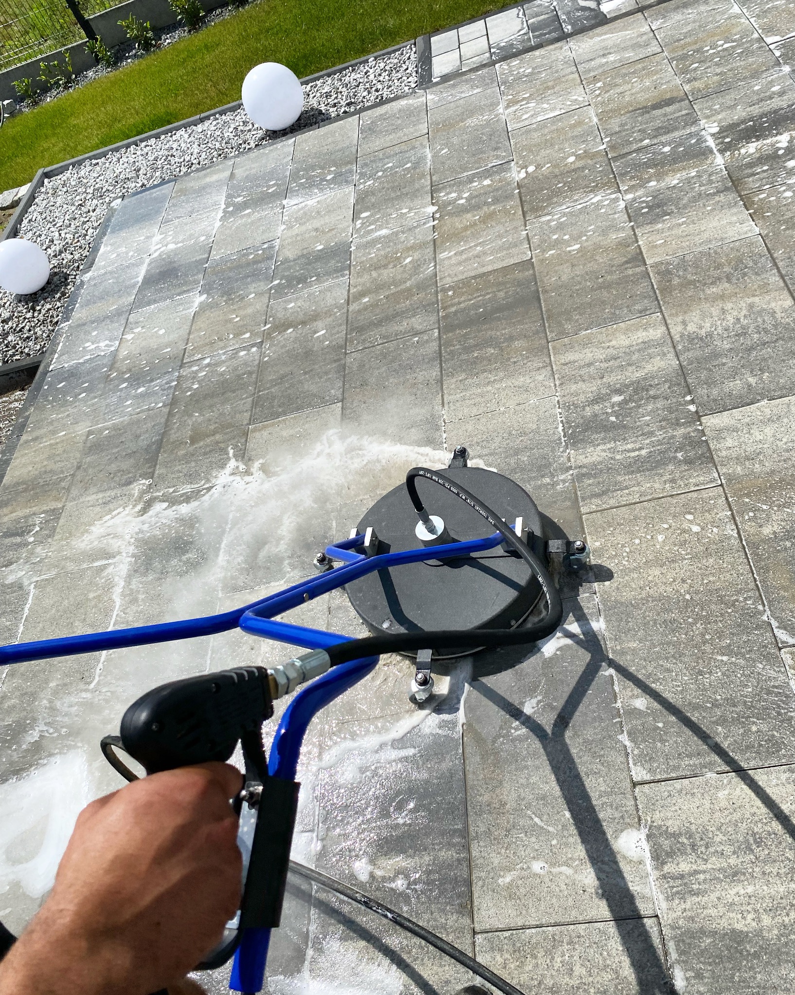 Mycie kostki brukowej urządzeniem z dyszą rotacyjną; widoczne białe kule dekoracyjne w tle.