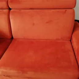 Pomarańczowa, aksamitna kanapa z regulowanym zagłówkiem, widoczne niewielkie plamy na siedzisku i oparciu.