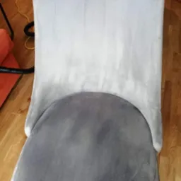 Krzesło tapicerowane z widoczną różnicą w czystości: górna część oparcia po praniu jest jaśniejsza i czystsza niż dolna część i siedzisko, z boku widoczny odkurzacz piorący.