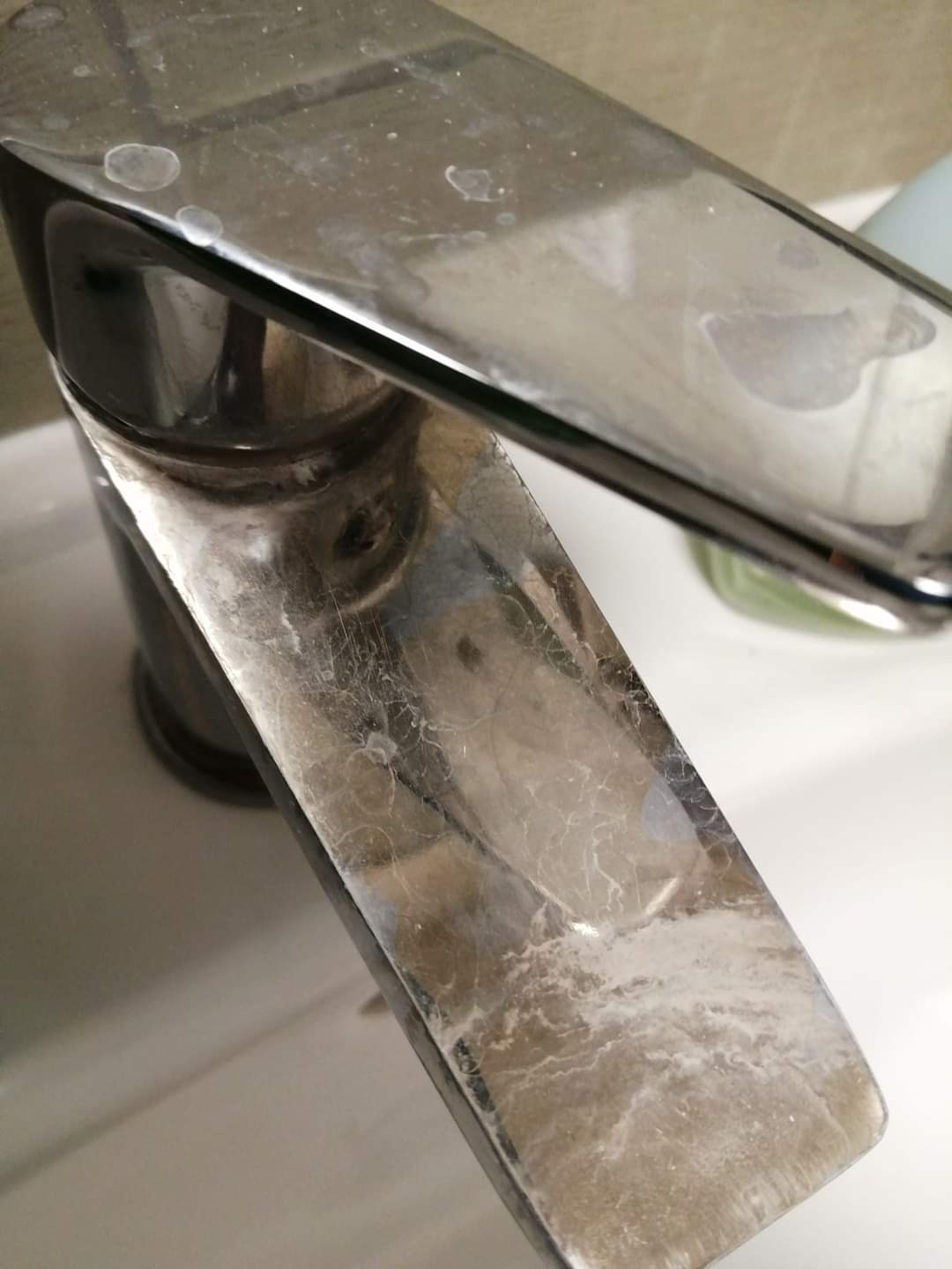 Bateria umywalkowa z wyraźnymi śladami osadu z kamienia i zaciekami po wodzie, widoczne z bliska na białym tle umywalki.