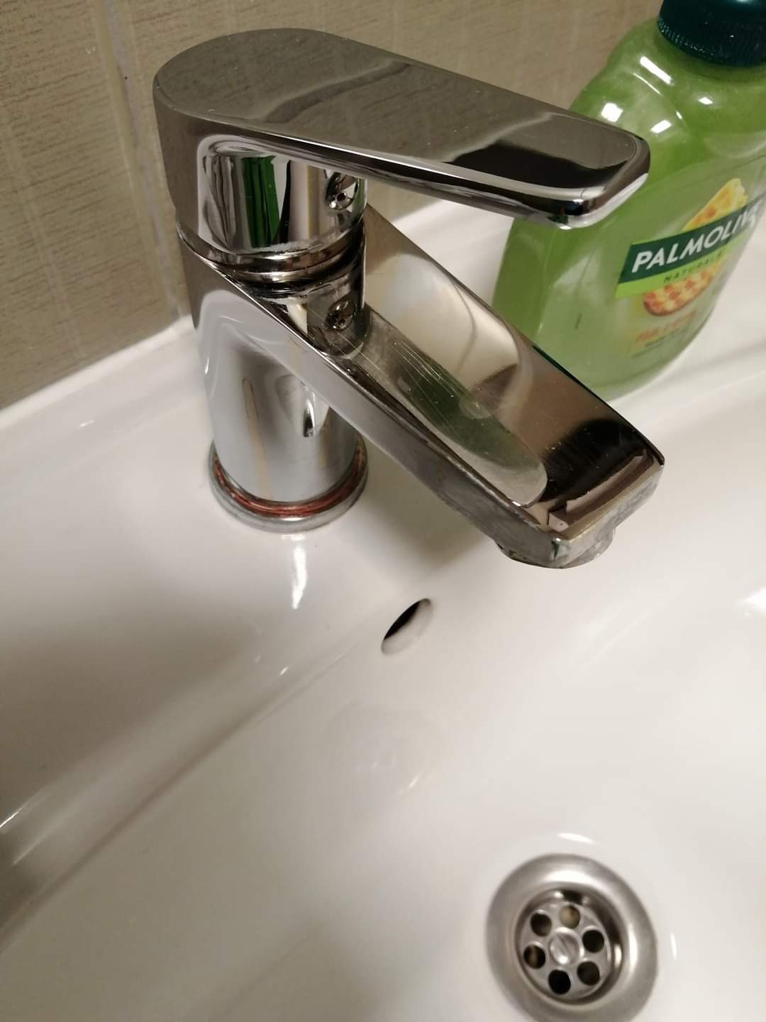 Bateria umywalkowa chromowana z niewielkimi śladami użytkowania, obok butelka mydła Palmolive na białej umywalce.