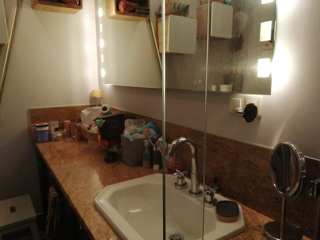 Umywalka z marmurowym blatem, zagracona różnymi przedmiotami codziennego użytku, widok z perspektywy osoby stojącej przed nią.