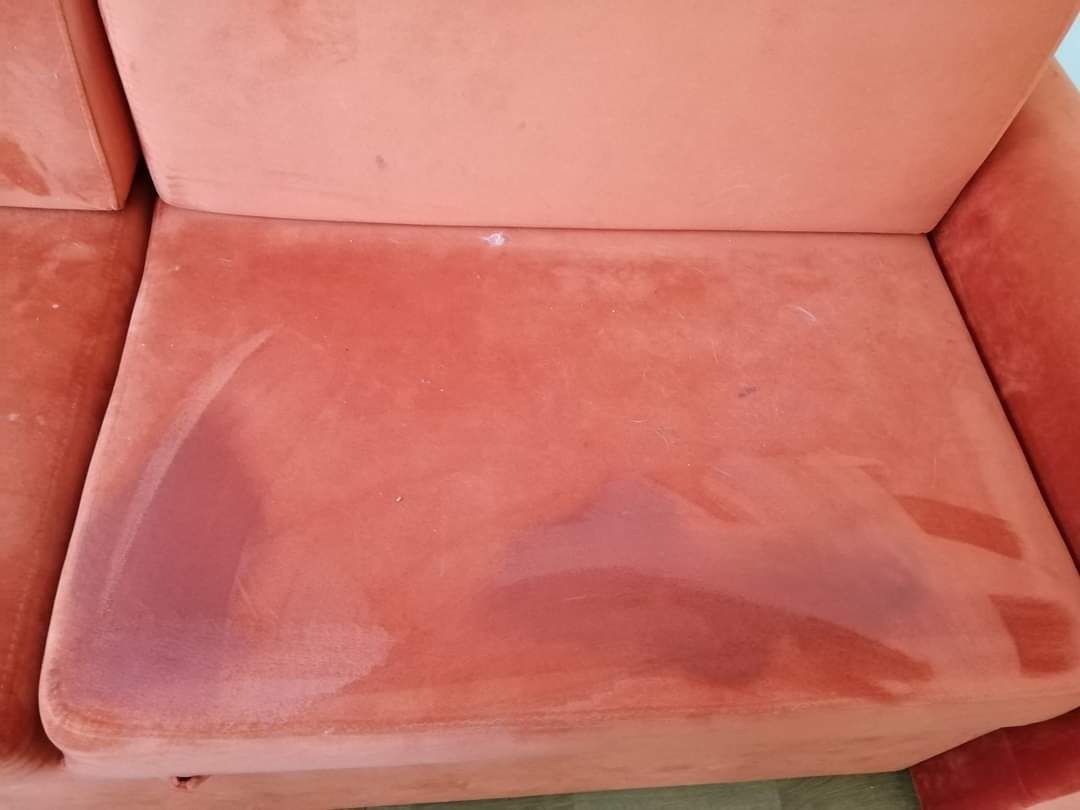 Fragment pomarańczowej kanapy z widocznymi plamami i śladami po czyszczeniu, ukazujący efekt odświeżenia tapicerki.