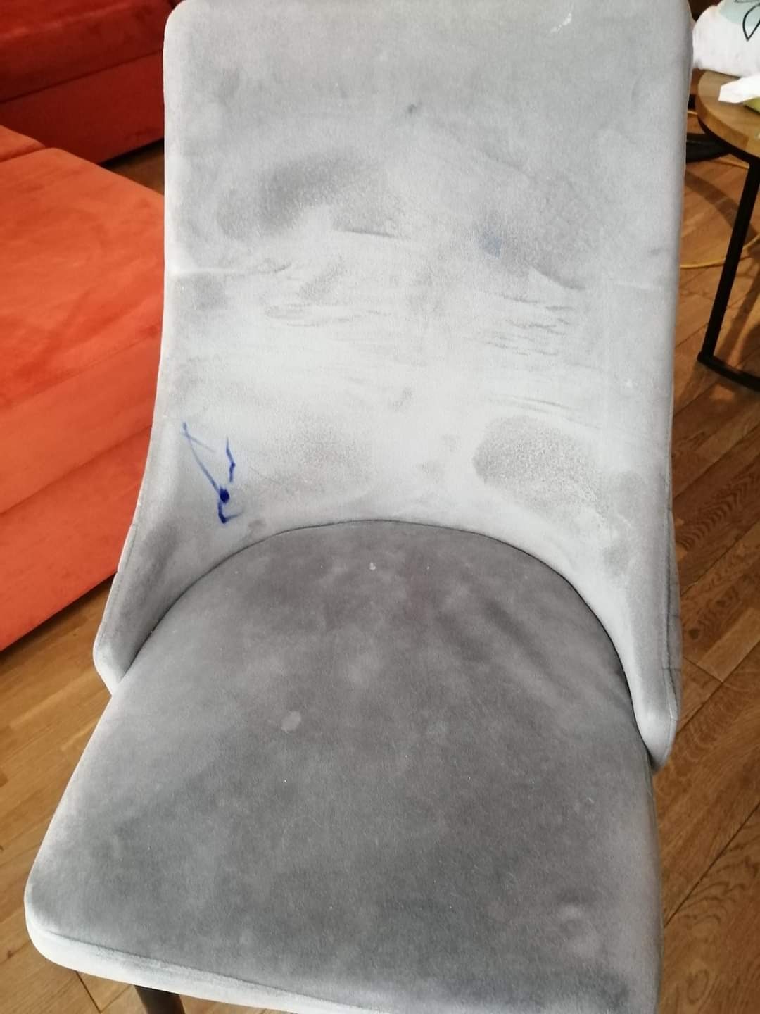 Szare krzesło tapicerowane z widocznymi plamami i śladami po czyszczeniu, z bliska, na drewnianej podłodze.