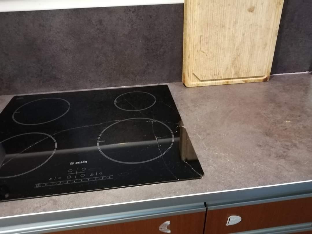 Pęknięta płyta indukcyjna marki Bosch na brązowym blacie kuchennym, obok deska do krojenia.