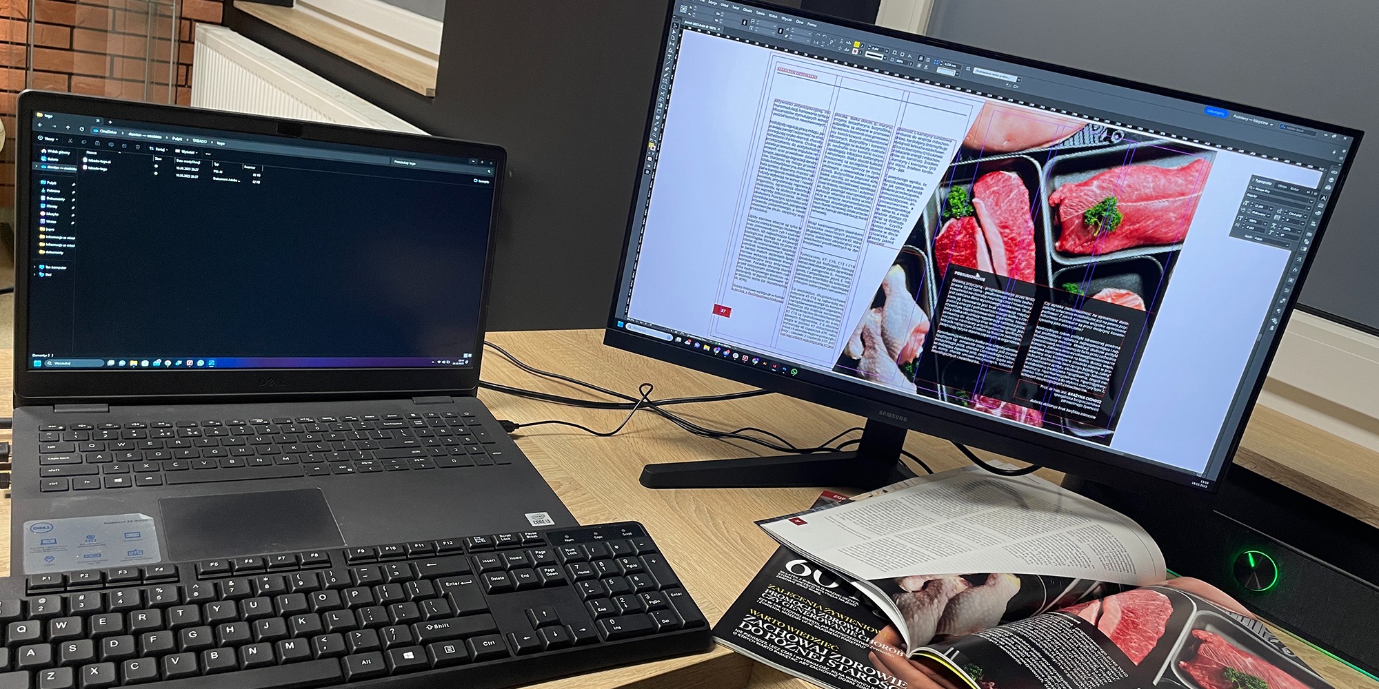Stanowisko pracy grafika: laptop z otwartym folderem, monitor wyświetlający projekt graficzny z artykułem o mięsie, obok leży otwarty magazyn z podobną tematyką.