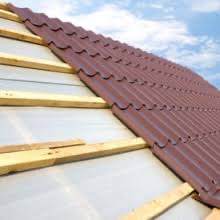 Fragment konstrukcji dachu z brązową blachodachówką ułożoną na łatach i kontrłatach, widoczna membrana dachowa, błękitne niebo w tle.