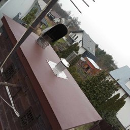 Dach As - Nowe, brązowe krycie dachu z kominem i odpowietrznikami na tle domów w Otwocku, widok z góry pod kątem.