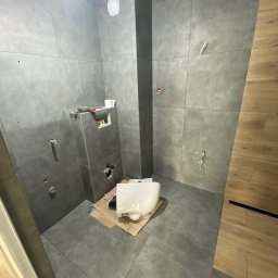 Modern Flat firma remontowa - Wnętrze łazienki w trakcie montażu podwieszanej toalety na tle szarych płytek; widoczne narzędzia i instalacje.