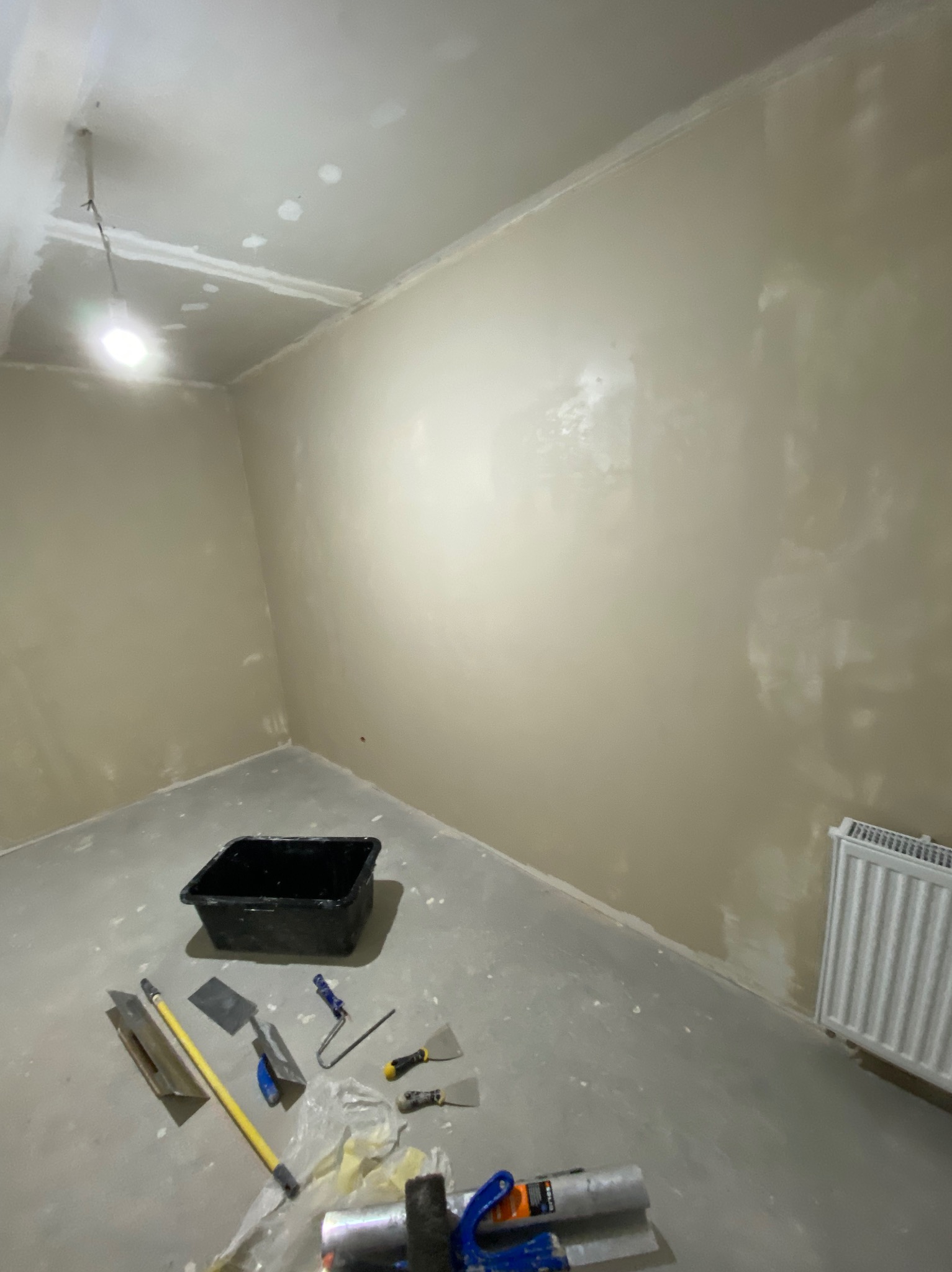 Pokój w trakcie szpachlowania w Sosnowcu, widoczne narzędzia: szpachelki, wałek, kuweta, ściany pokryte wstępną warstwą gładzi, grzejnik w rogu pomieszczenia.