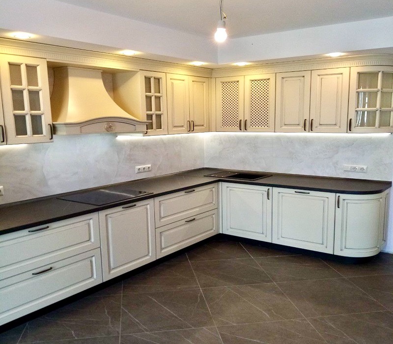 Jasna kuchnia z frezowanymi frontami, czarnym blatem i ażurowymi szafkami górnymi podświetlona ledami.