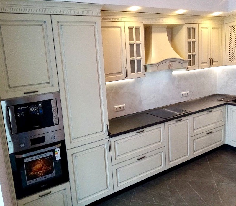 Klasyczna kuchnia w odcieniach kremu z ciemnym blatem, zabudowana z piekarnikiem i mikrofalówką Samsung, oświetlenie LED pod szafkami wiszącymi.