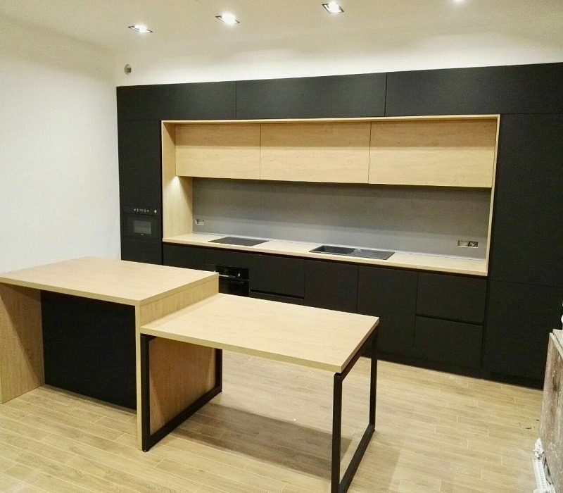 Nowoczesna kuchnia z czarnymi szafkami i jasnymi drewnianymi frontami górnymi, minimalistyczny design, wyspa kuchenna z blatem z jasnego drewna i czarną podstawą, stół z metalowymi nogami...