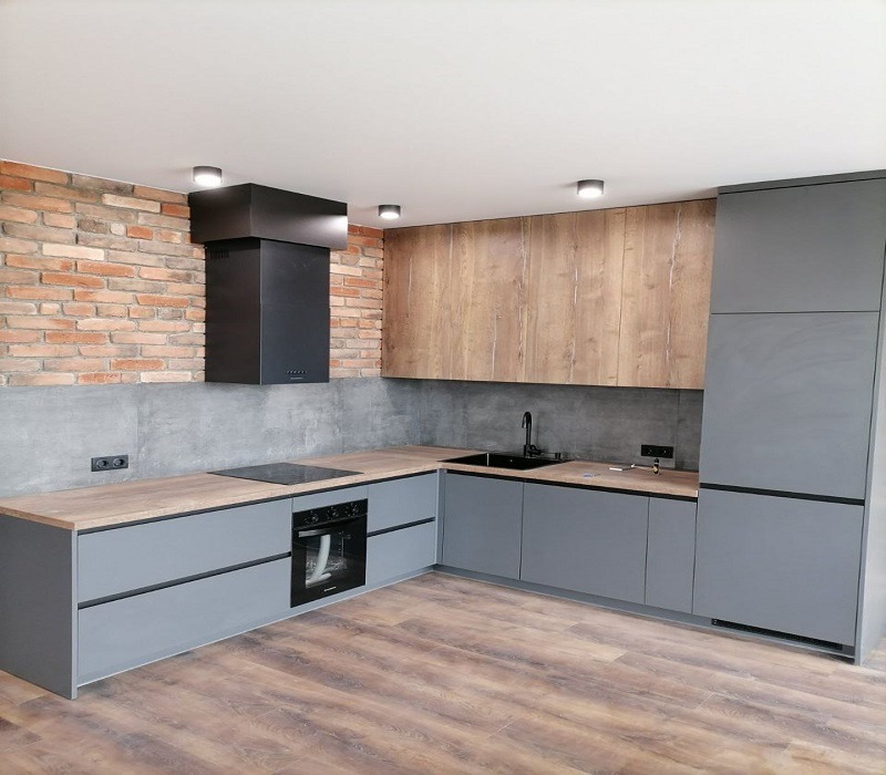 Nowoczesna kuchnia z szarymi szafkami dolnymi i drewnopodobnymi górnymi, czarnym okapem na tle ceglanej ściany i drewnianą podłogą.
