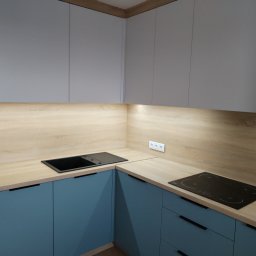 FUHP - Nowoczesna kuchnia narożna z szarymi szafkami górnymi i niebieskimi dolnymi, blatem imitującym jasne drewno oraz czarnym zlewem i płytą indukcyjną.