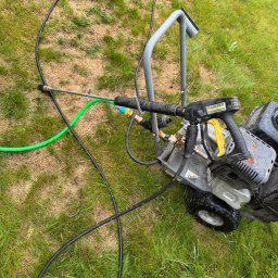 SpecGreen - Myjka ciśnieniowa Karcher Professional na trawie, z widocznymi przewodami i lancą. Sprzęt gotowy do użycia, leży na zielonej trawie.