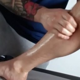 Skowron Med Inowrocław - Fizjoterapia - Rehabilitacja - Masaż - Masażysta dłonią masuje łydkę pacjenta posmarowaną olejkiem, widoczny fragment tatuażu na ramieniu masażysty.