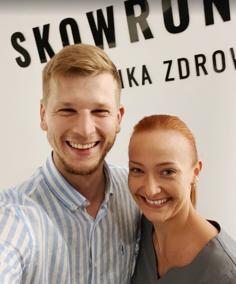 Uśmiechnięci pracownicy kliniki zdrowia 'Skowronek' pozują do zdjęcia na tle logo firmy.