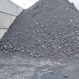 PRODUKCJA HANDEL USŁUGI PORA BOGUMIŁ PORA - Góra ekogroszku o frakcji mieszanej z widocznymi bryłkami różnej wielkości, ułożona przy betonowych płytach.