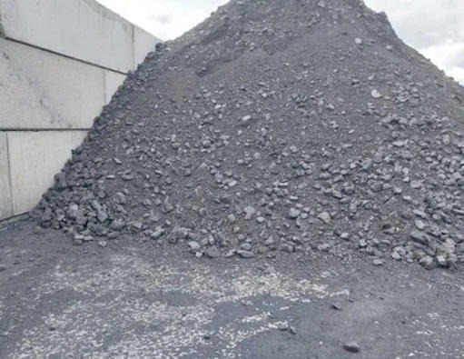 Góra ekogroszku o frakcji mieszanej z widocznymi bryłkami różnej wielkości, ułożona przy betonowych płytach.