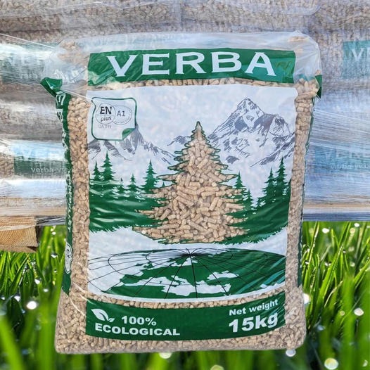 Worek pelletu drzewnego VERBA 15kg z certyfikatem DIN PLUS A1, na tle imitacji trawy i palety, z widocznym motywem górskim i drzew iglastych na opakowaniu.
