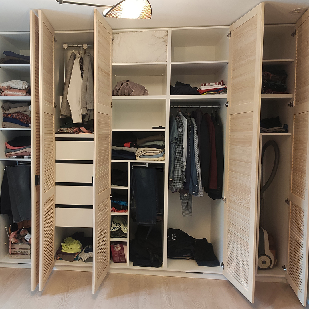 Otwarta, trzydrzwiowa szafa z jasnego drewna z lamelowymi frontami, widoczne ubrania, półki i szuflady, w Krygu.