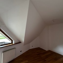 F.H.U ADMA Adam Grygier - Poddasze po malowaniu: białe ściany, drewniana podłoga, okno trójkątne z widokiem na zewnątrz, grzejnik pod oknem. Minimalistyczny styl, świeżo po remoncie.