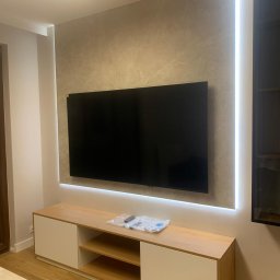 Bohdan Ostradchuk - Wykończona ściana TV z podświetleniem LED. Marmurowa faktura ściany i szafka RTV w odcieniach drewna. Nowoczesny design wnętrza, widok z perspektywy lekko z dołu.