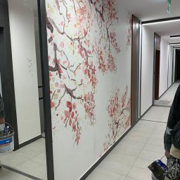 Bohdan Ostradchuk - Korytarz biurowy po malowaniu z motywem kwiatowym. Widoczny fragment osoby z narzędziami malarskimi, podkreślający realizację usługi malarskiej.