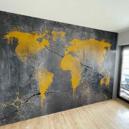 Bohdan Ostradchuk - Ściana z mapą świata w odcieniach szarości i złota, stylizowana na popękaną powierzchnię. Widoczny kompas w lewym dolnym rogu i drewniana podłoga.