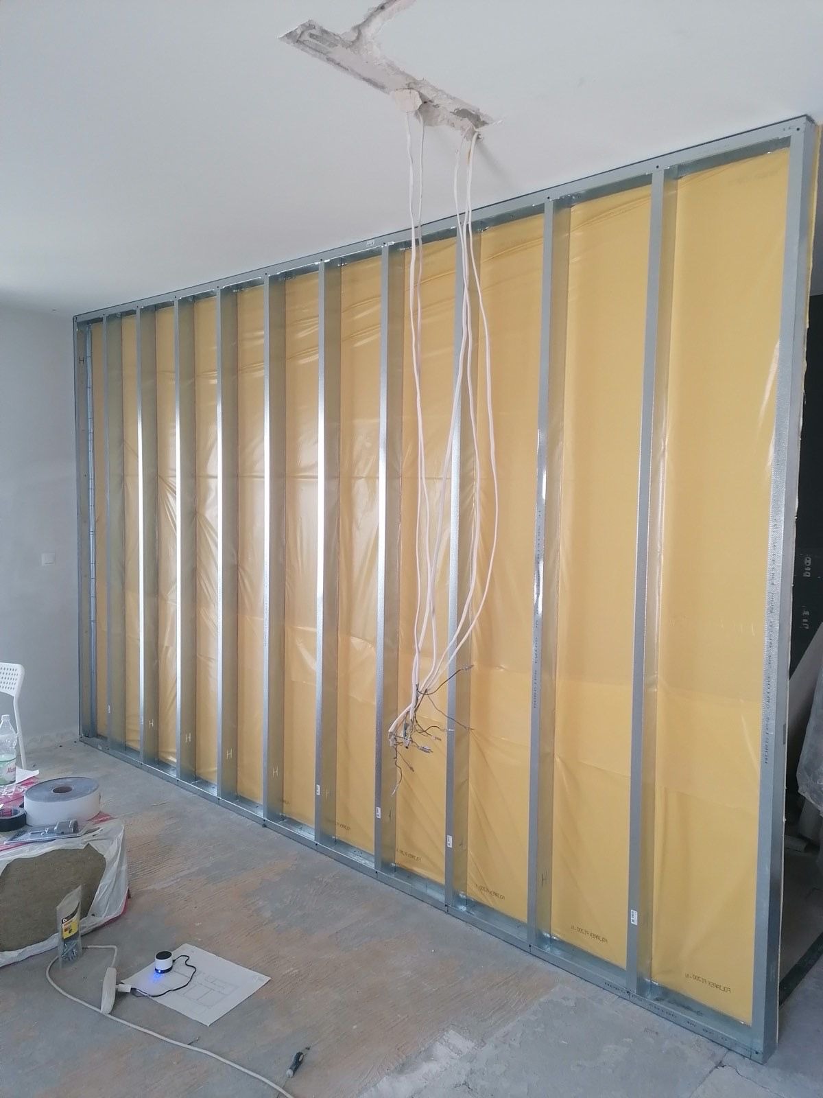 Konstrukcja ściany działowej z profili stalowych i folii paroizolacyjnej, widoczne przewody elektryczne, przygotowanie do montażu płyt gipsowo-kartonowych.