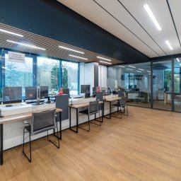 COMEX SPÓŁKA Z OGRANICZONĄ ODPOWIEDZIALNOŚCIĄ - Nowoczesne biuro z drewnianą podłogą, stanowiskami pracy wzdłuż okna i ekspozycją próbek materiałów wykończeniowych.