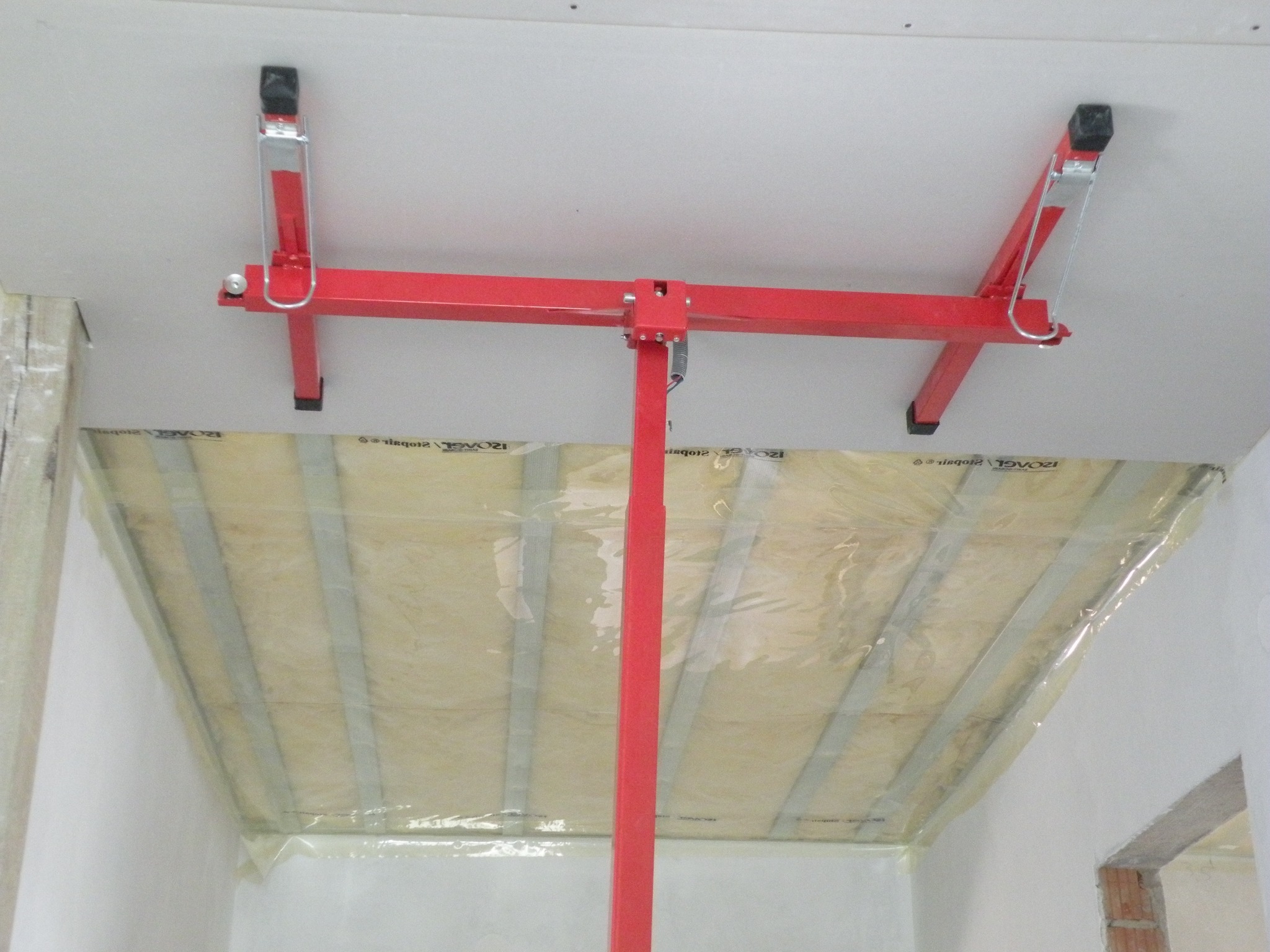 Czerwony podnośnik do płyt gipsowo-kartonowych podtrzymujący izolację poddasza, zabezpieczoną folią, przed montażem płyt.