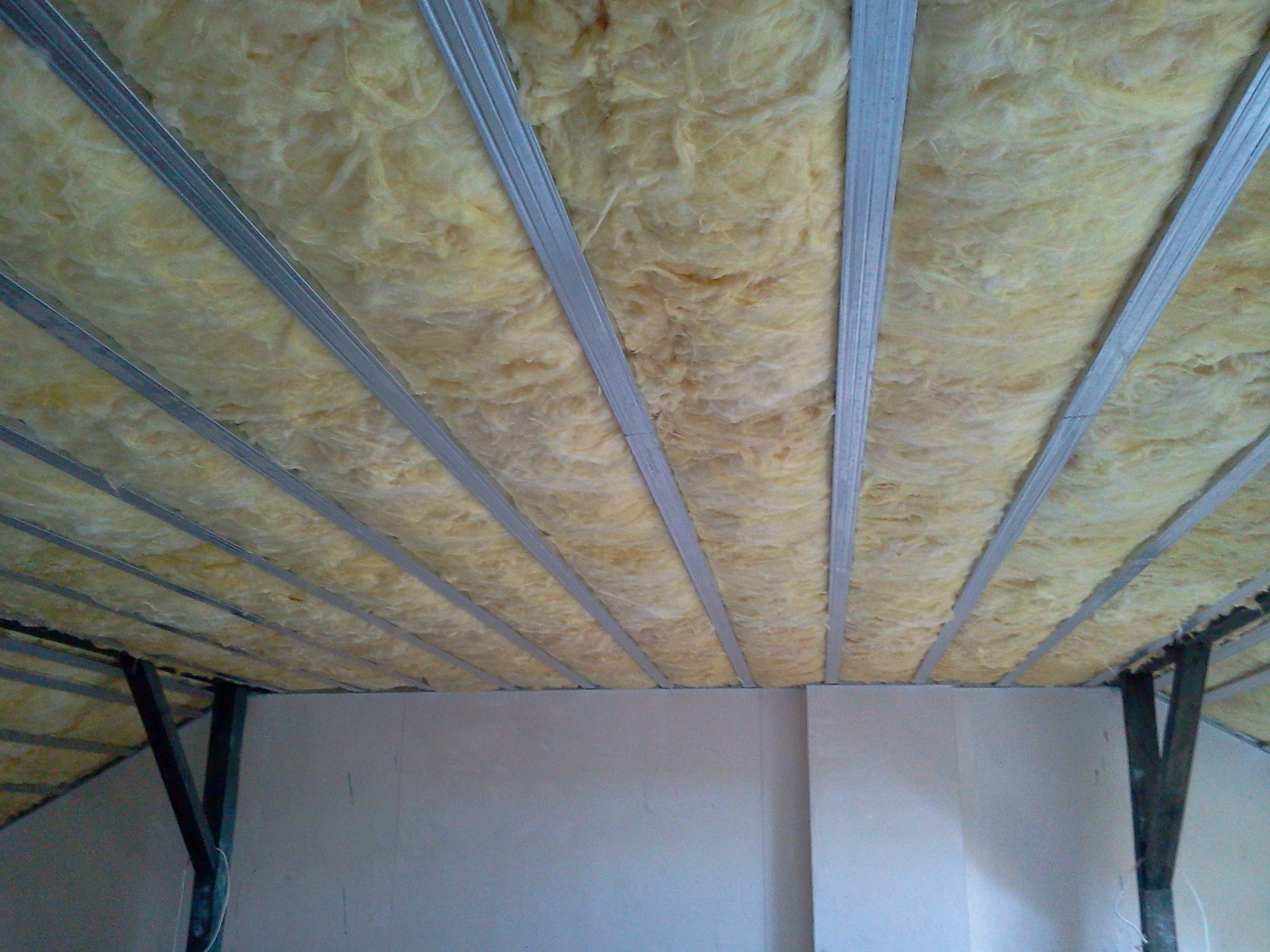 Poddasze z widoczną izolacją z wełny mineralnej, zamontowaną między metalowymi profilami konstrukcyjnymi, przed zakryciem płytami gipsowo-kartonowymi.