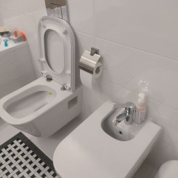 Paving House - Nowoczesna, biała łazienka z podwieszaną toaletą z otwartą deską i bidetem, białe płytki na ścianach, czarno-biała mozaika na podłodze, minimalistyczny styl.